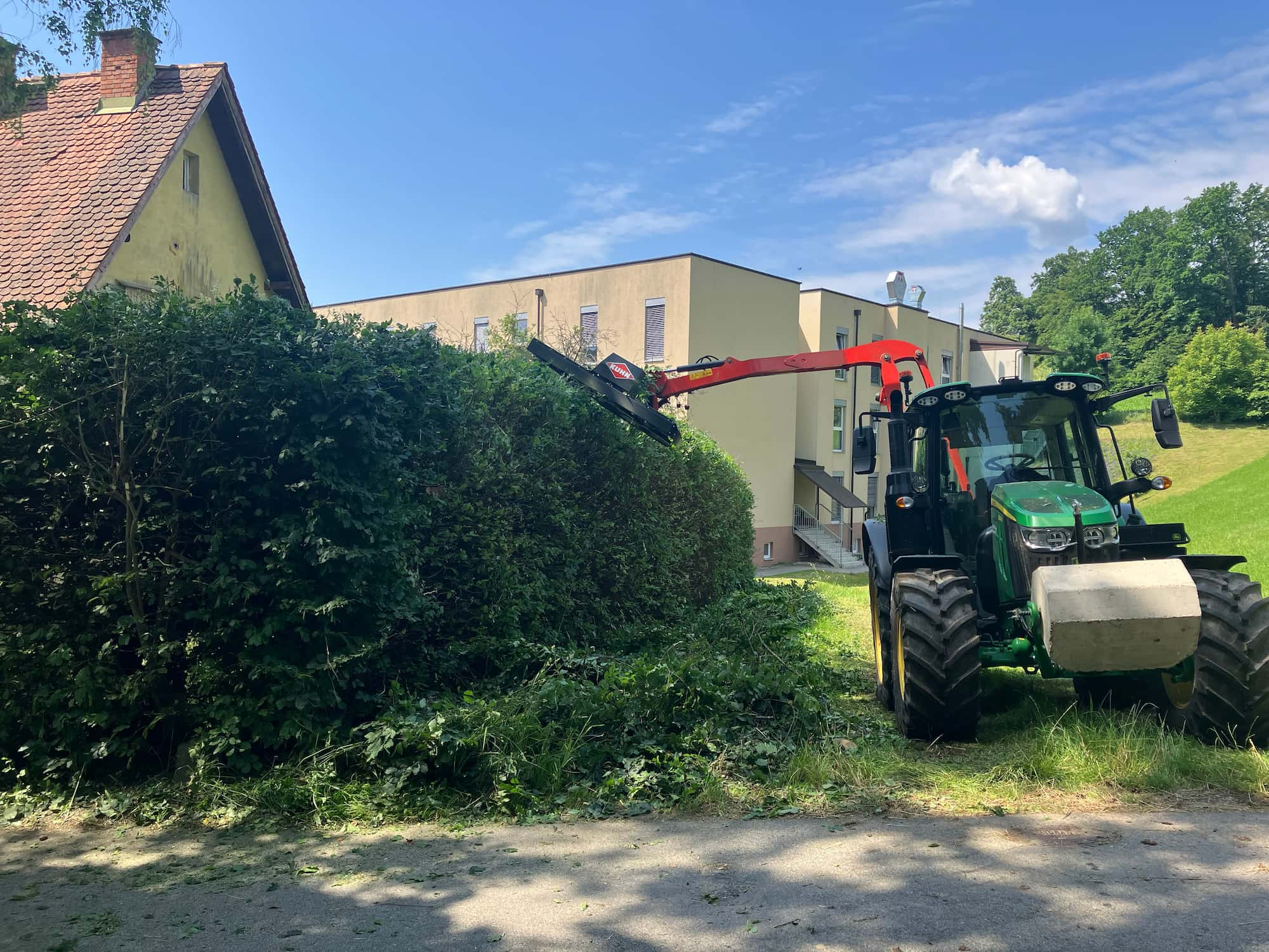 Das Bild zeigt einen Traktor, der eine Hecke schneidet.