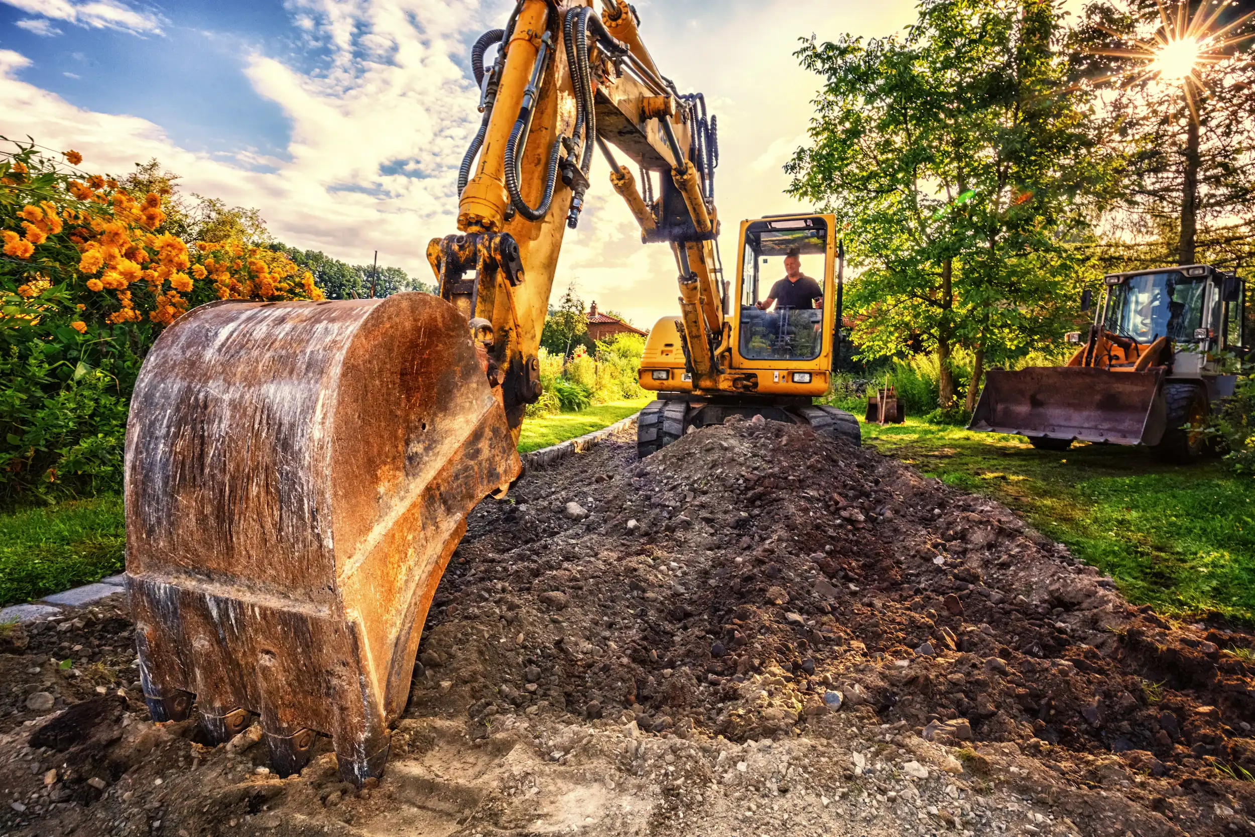 Das Bild zeigt einen gelben Bagger, der einen Garten umgräbt. Es soll für Landschafts- und Gartengestaltung stehen.